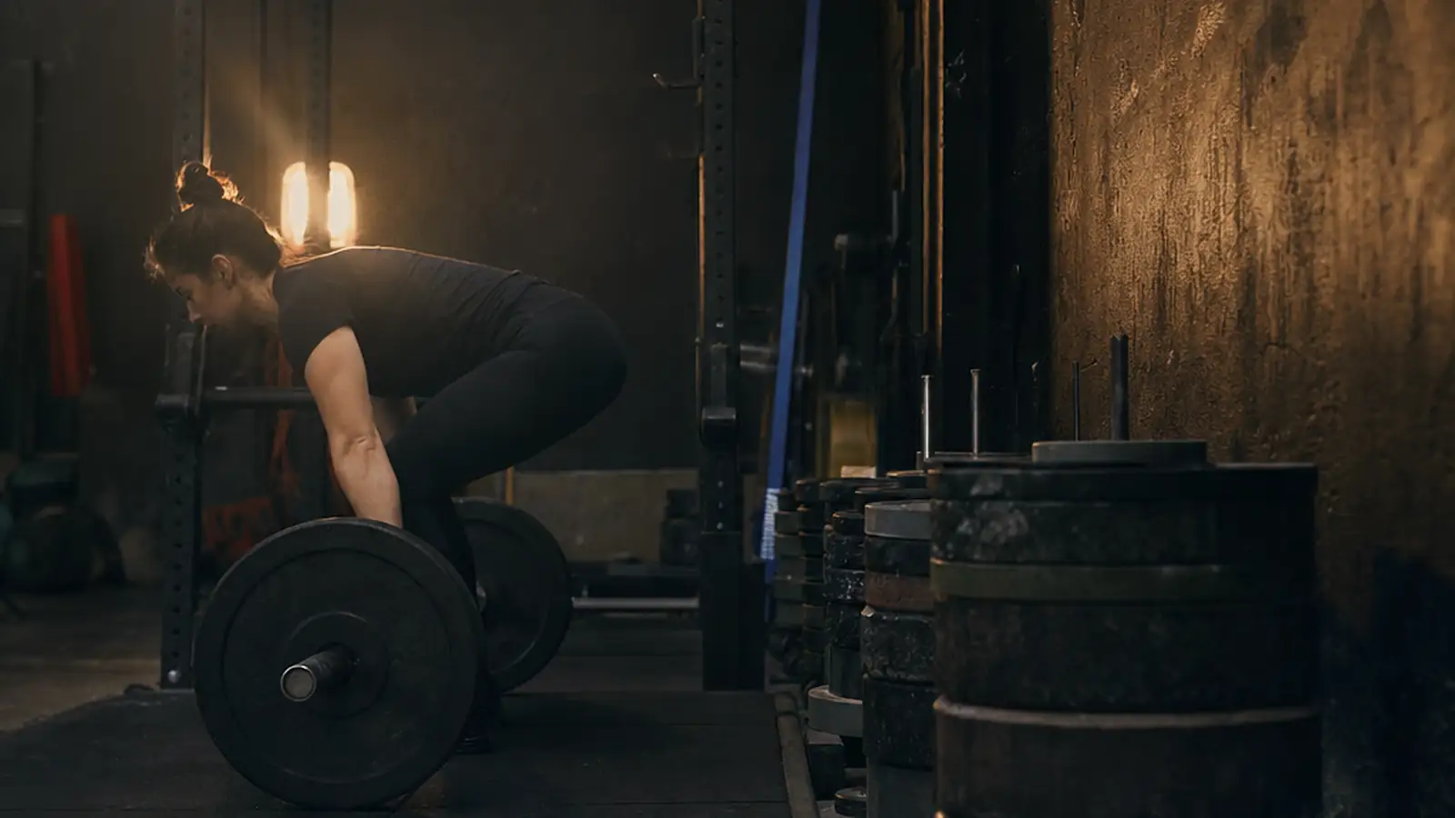 A woman sets up for a deadlift on a rubber platform, chalked hands on the bar.